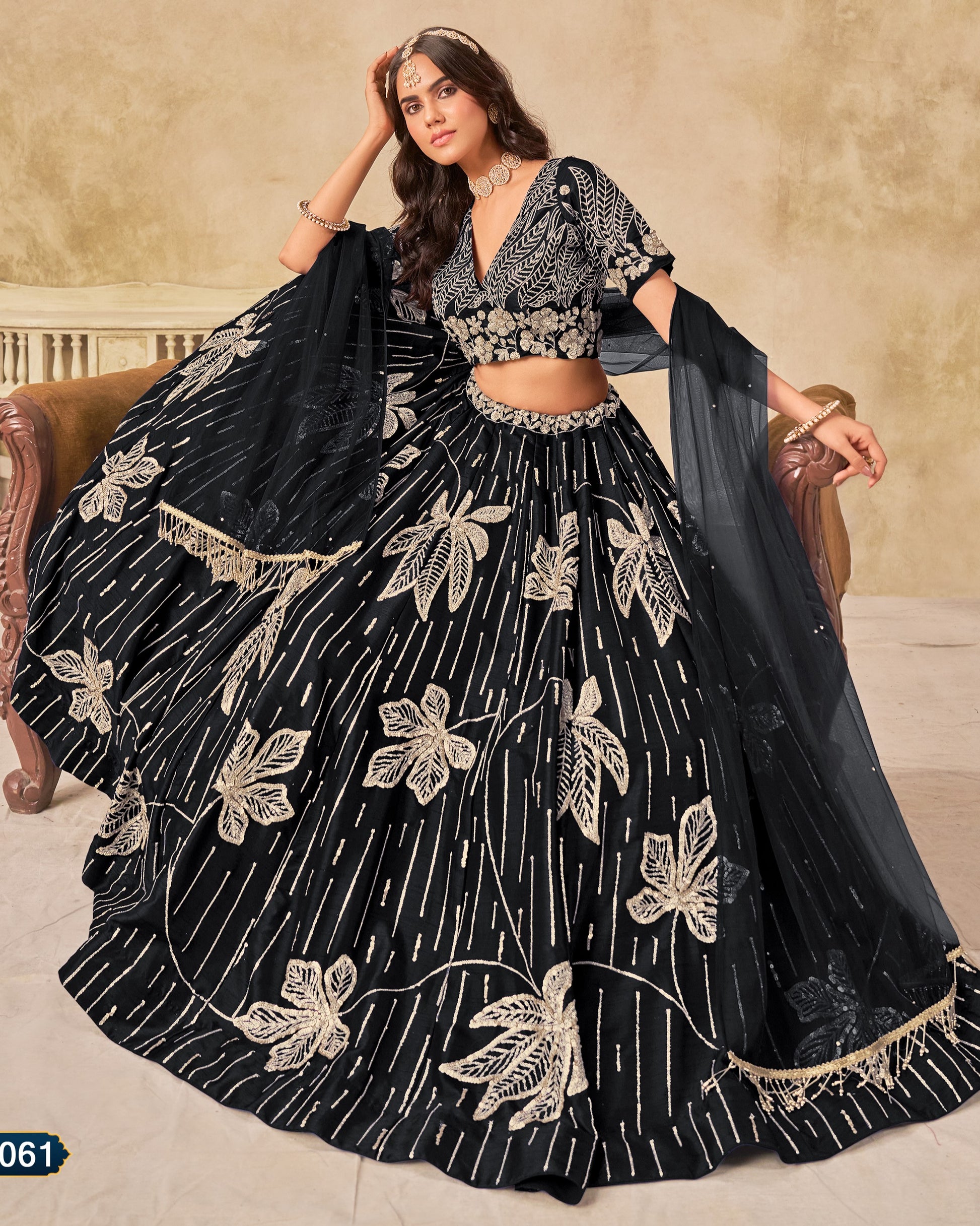 Woman wearing a black and gold embroidered lehenga sitting on a couch.