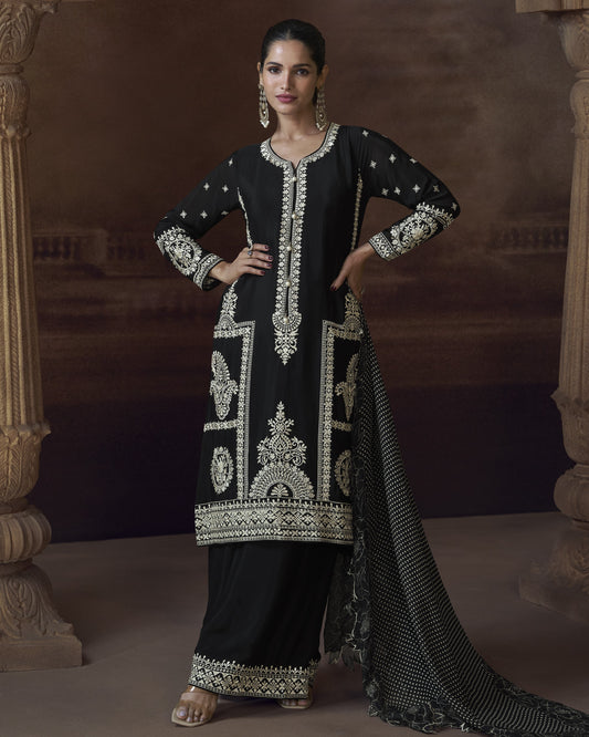 Woman wearing a black traditional outfit with intricate white embroidery in a decorative setting.