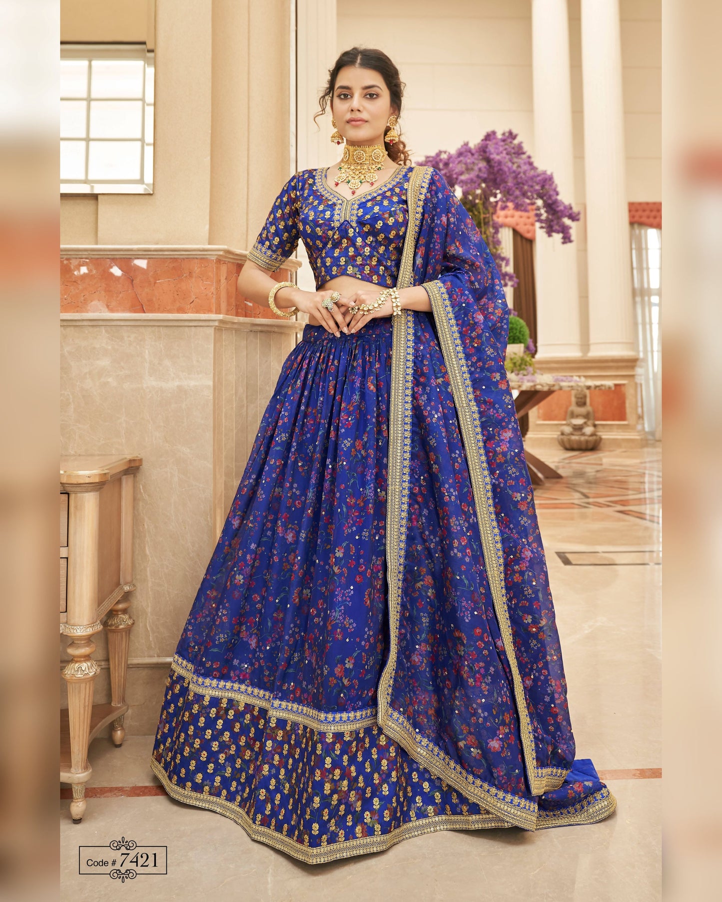 Woman wearing a blue traditional outfit with intricate patterns in an indoor setting.