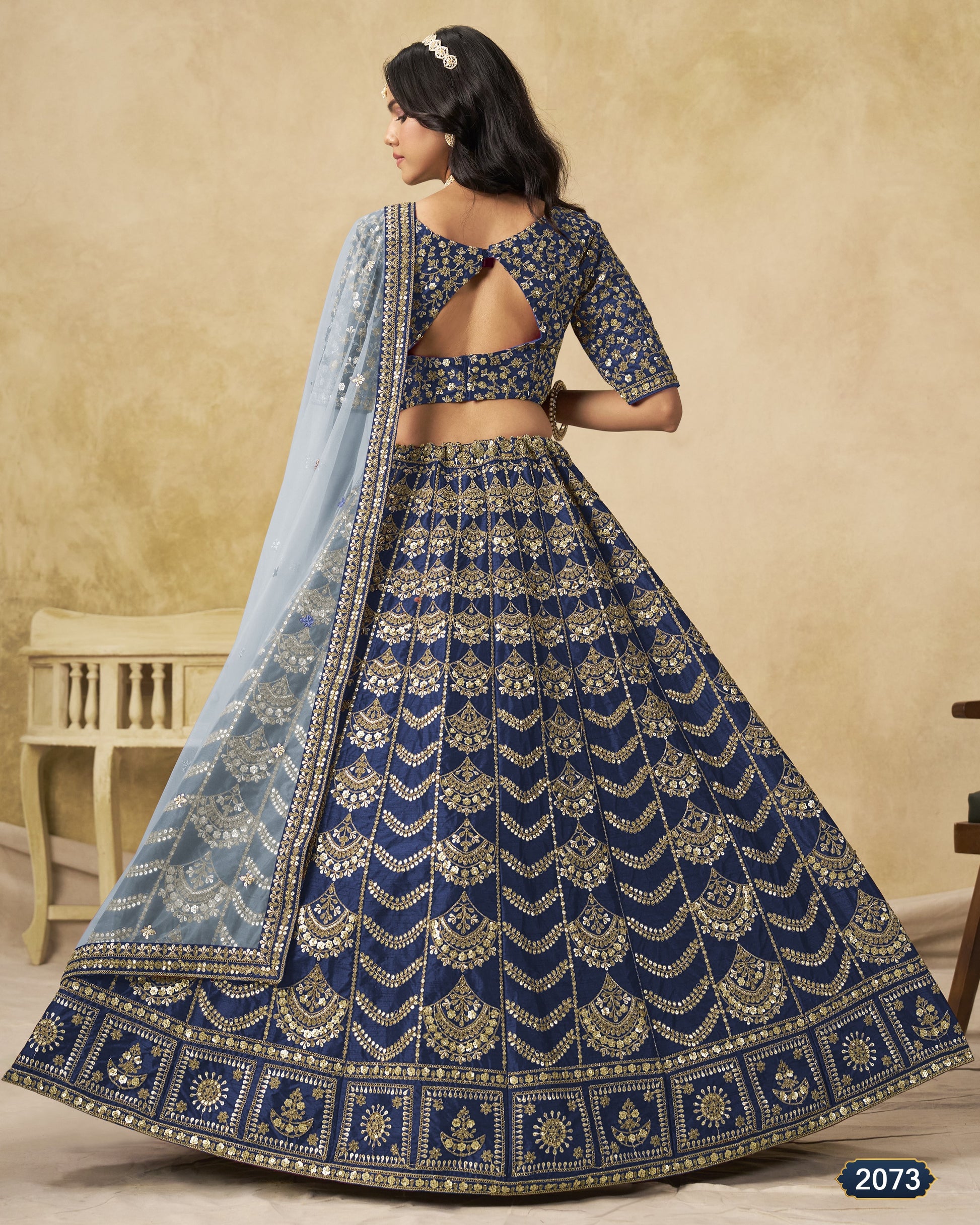 Woman wearing a blue embroidered lehenga with a matching dupatta against a beige background