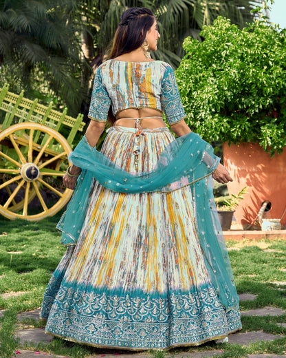 Woman in a traditional outfit with a colorful dress and blue dupatta in an outdoor setting.