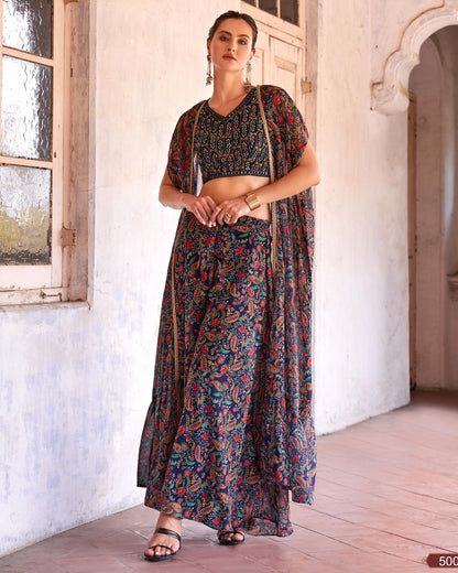 Woman in a floral saree standing in a sunlit room with white walls and wooden floor.