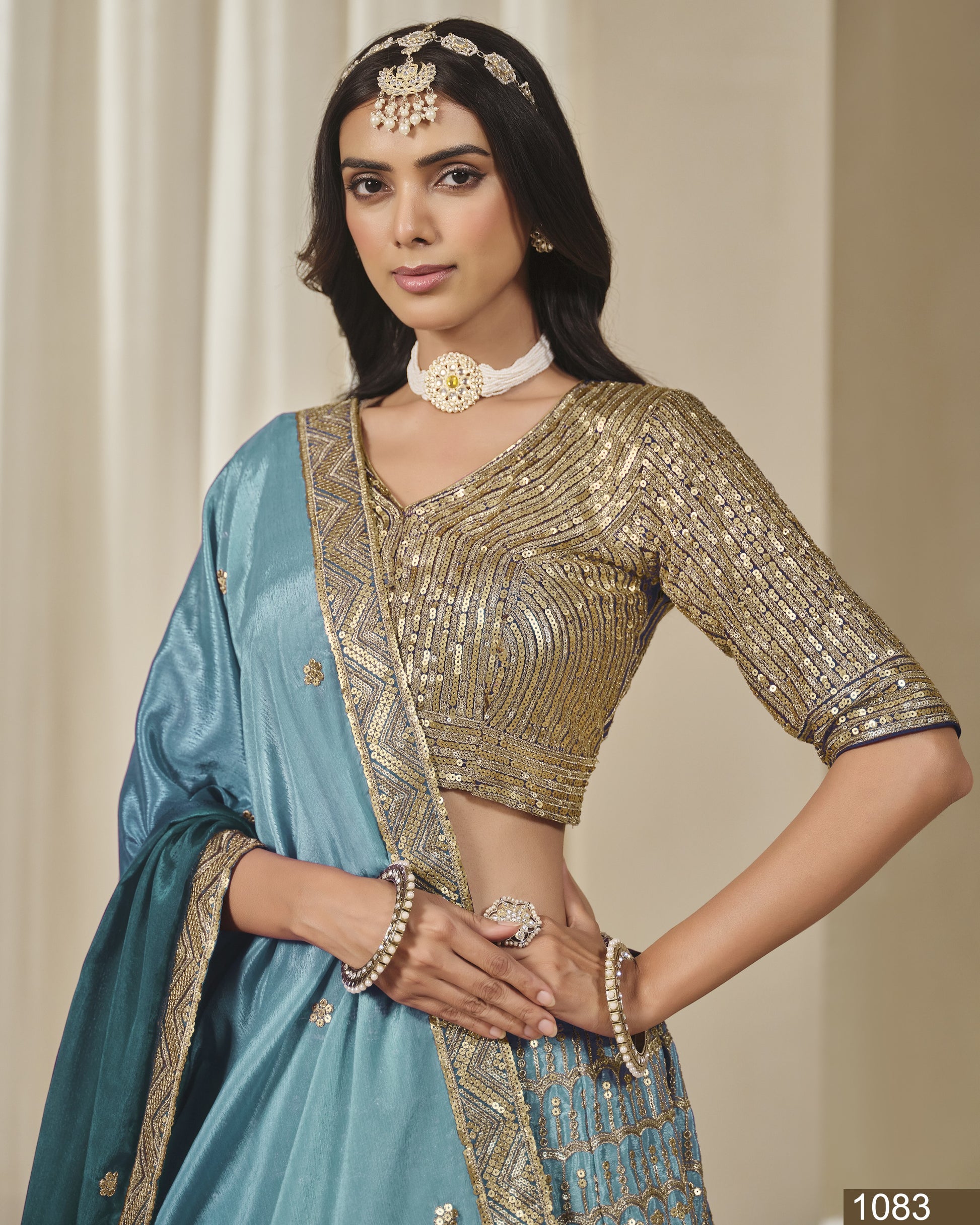Woman wearing a traditional outfit with a blue saree and gold blouse against a neutral background
