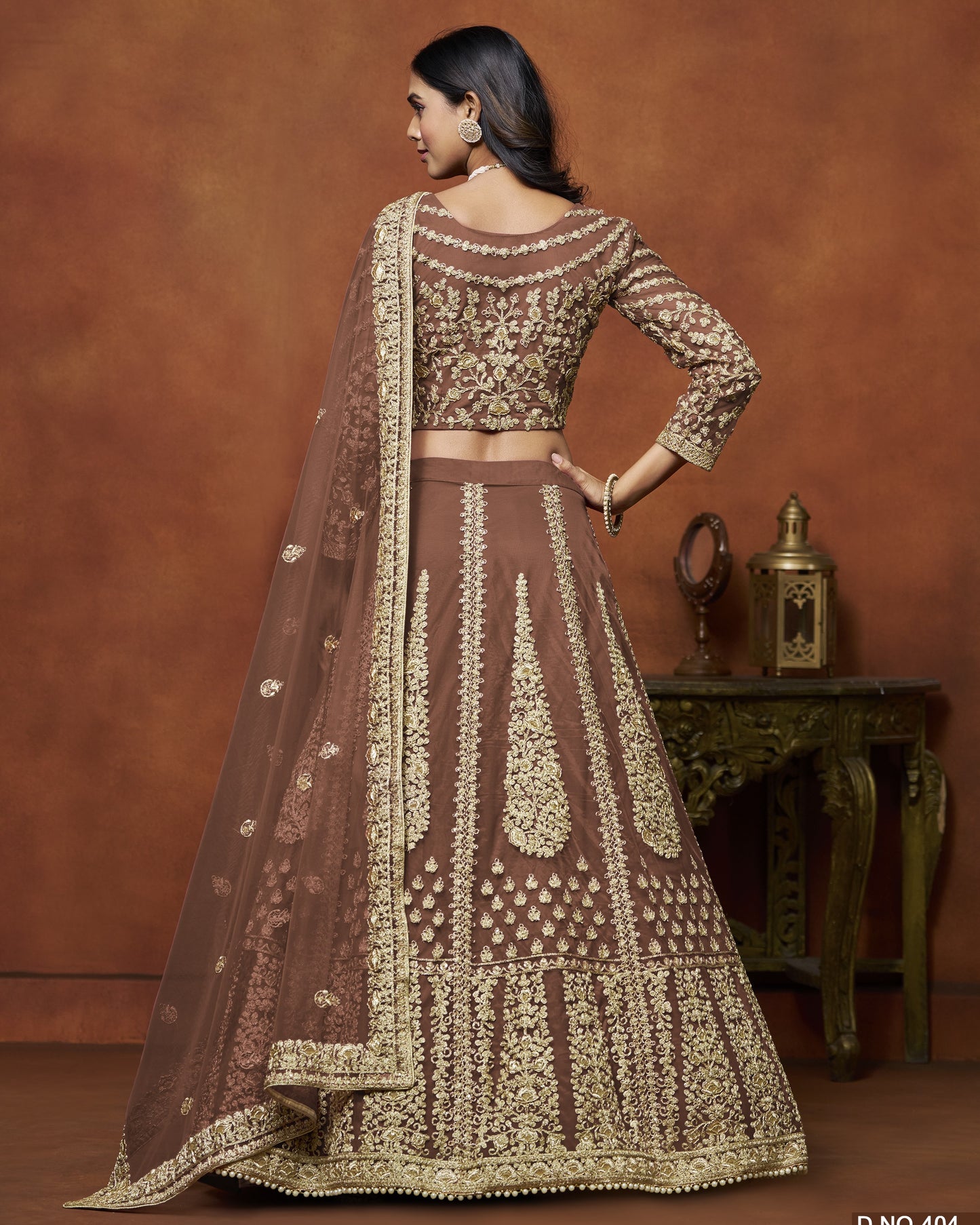 Woman wearing a brown and gold embroidered traditional outfit against a brown background