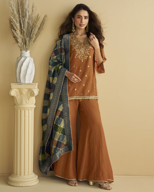 Woman in a brown outfit with a patterned shawl standing next to a decorative column.