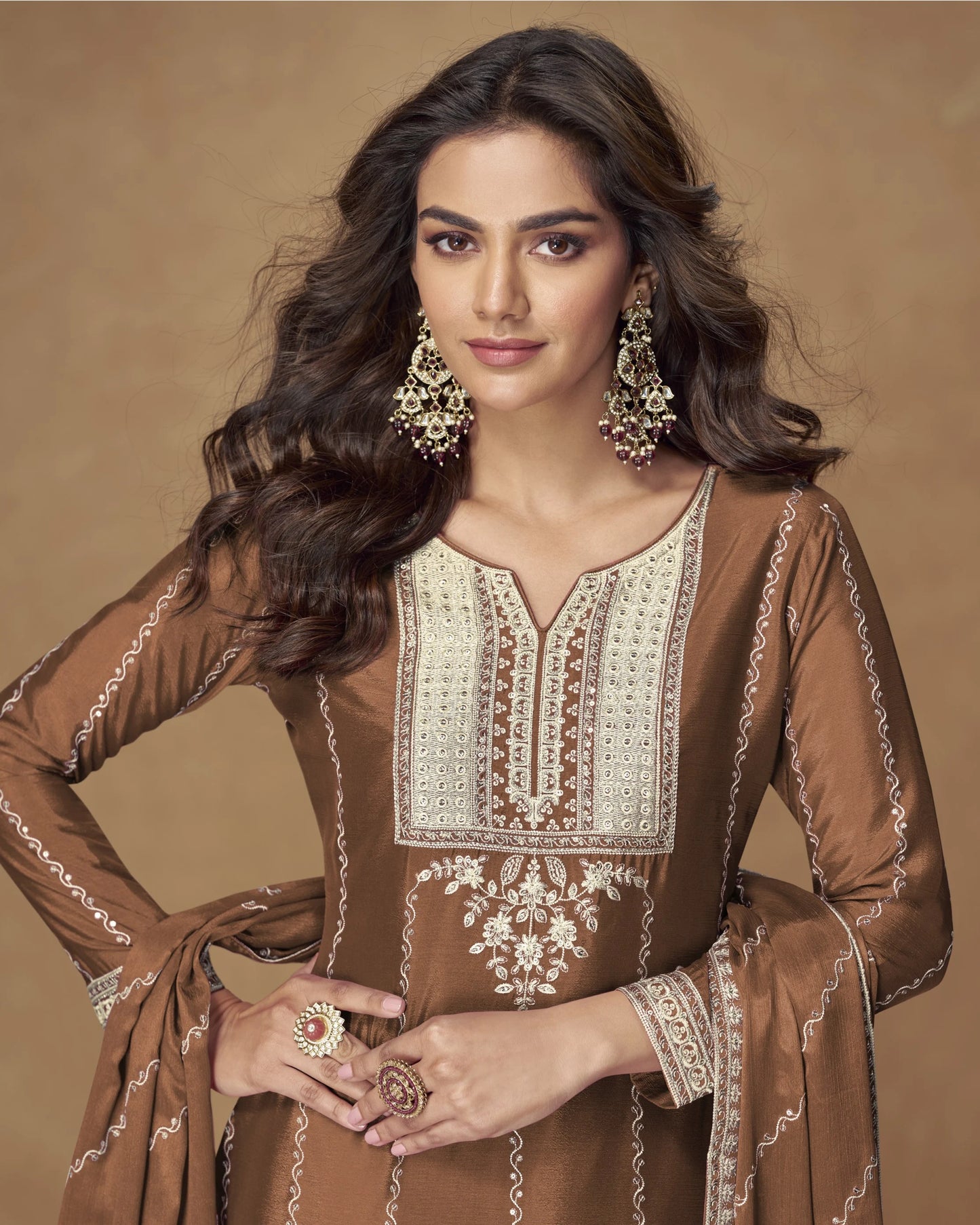 Woman wearing a brown embroidered traditional outfit with jewelry on a beige background