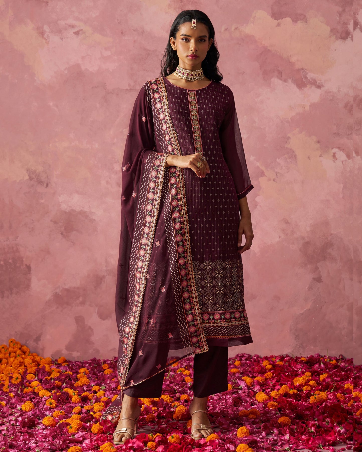 Woman in a traditional outfit standing on flower petals with a pink floral background