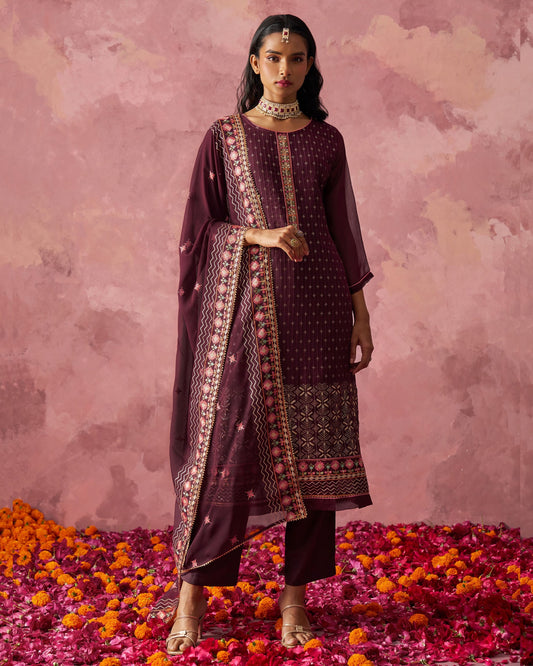 Woman in a traditional outfit standing on flower petals with a pink floral background