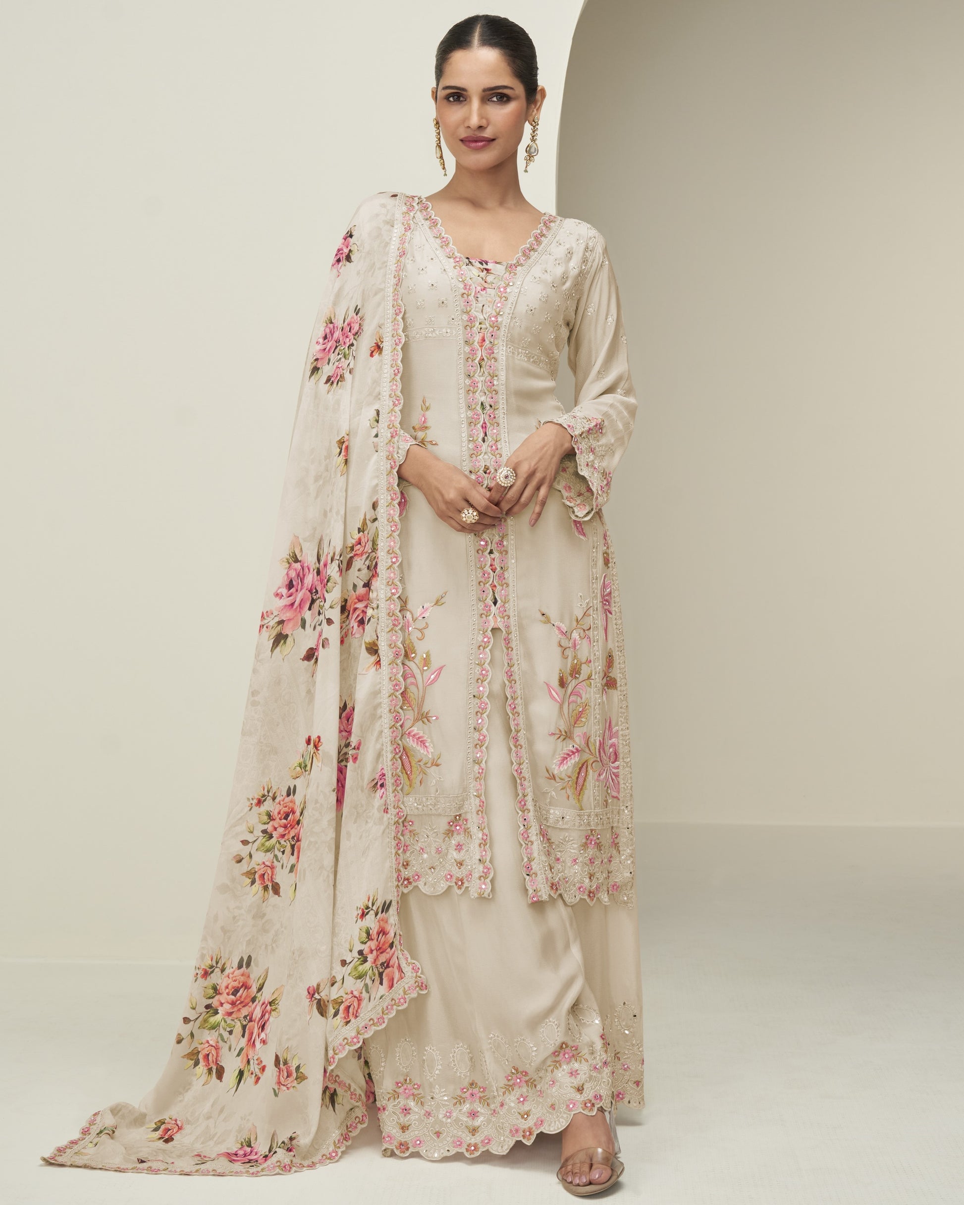 Woman wearing a floral embroidered outfit with a matching dupatta on a plain background