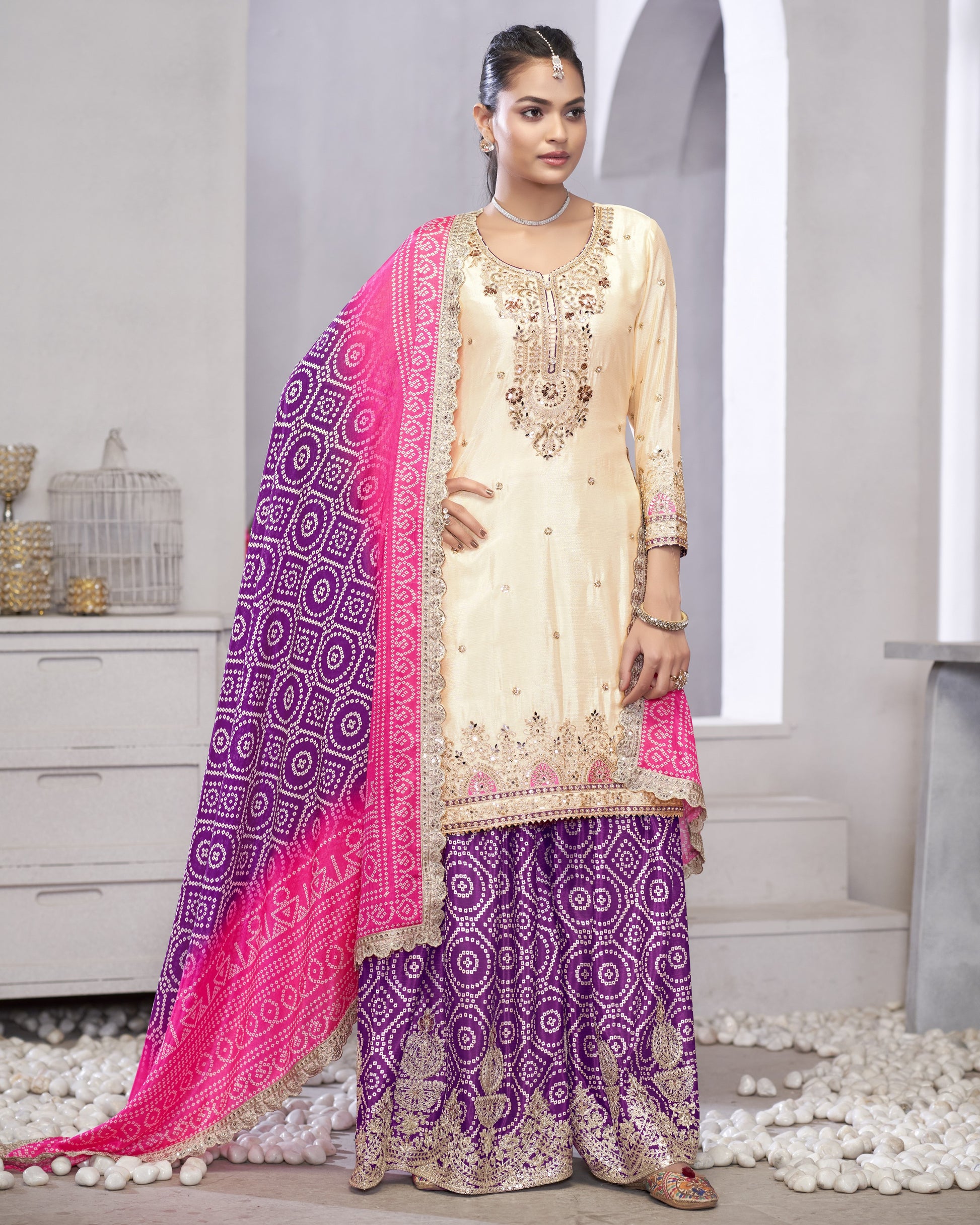 Woman wearing a traditional outfit with a pink and purple dupatta in a minimalistic setting.