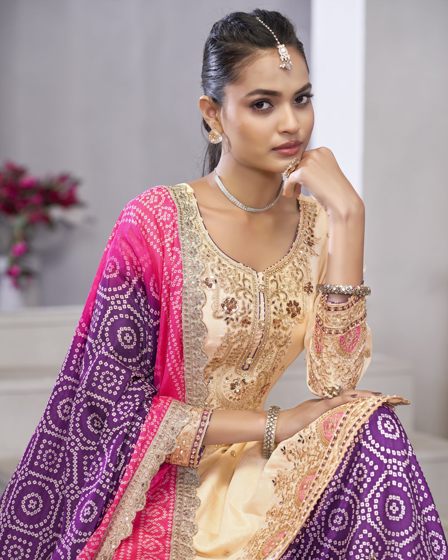 Woman wearing a traditional outfit with pink and purple dupatta and gold embroidery.