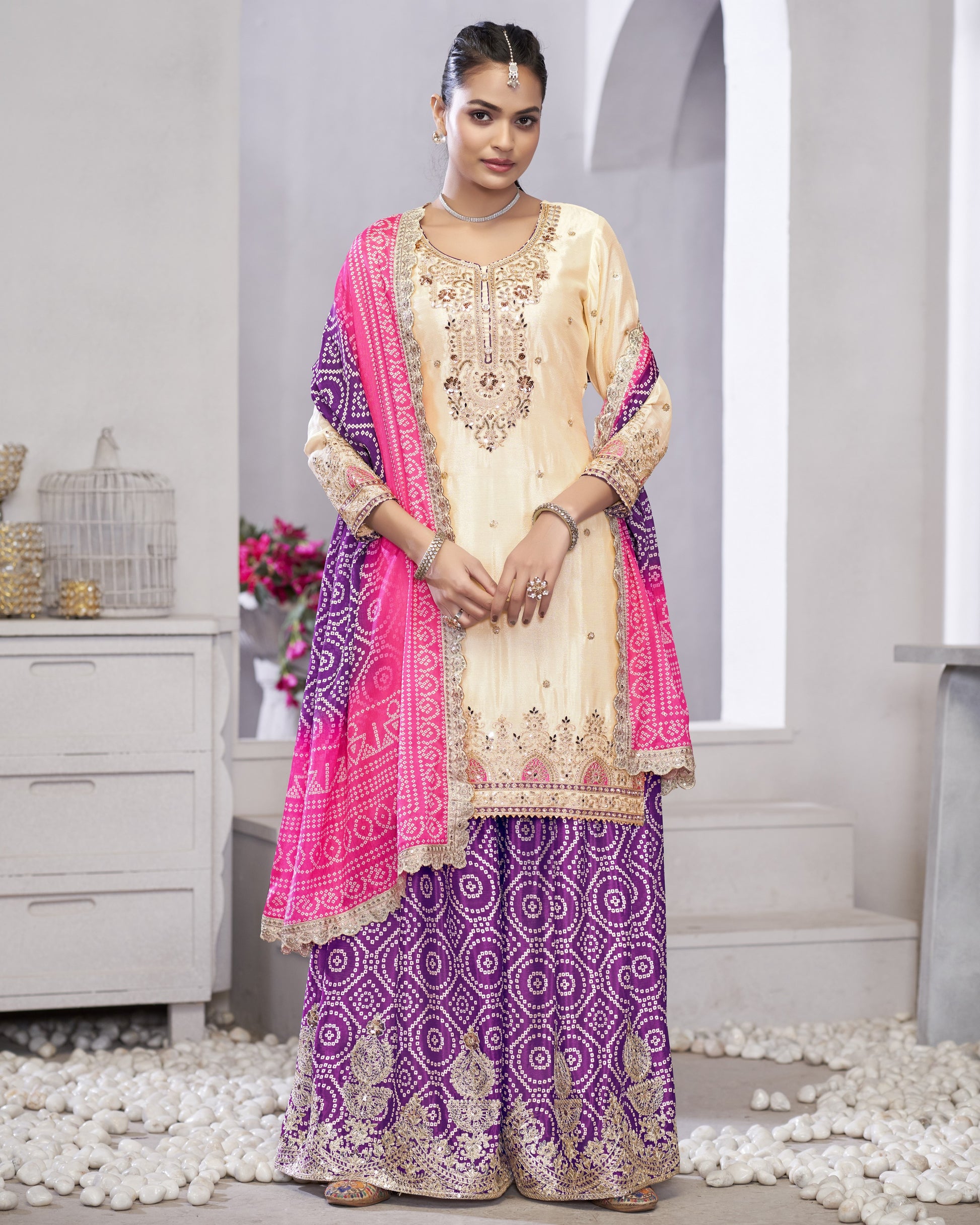 Woman wearing a traditional outfit with a pink and purple dupatta in a minimalistic setting.