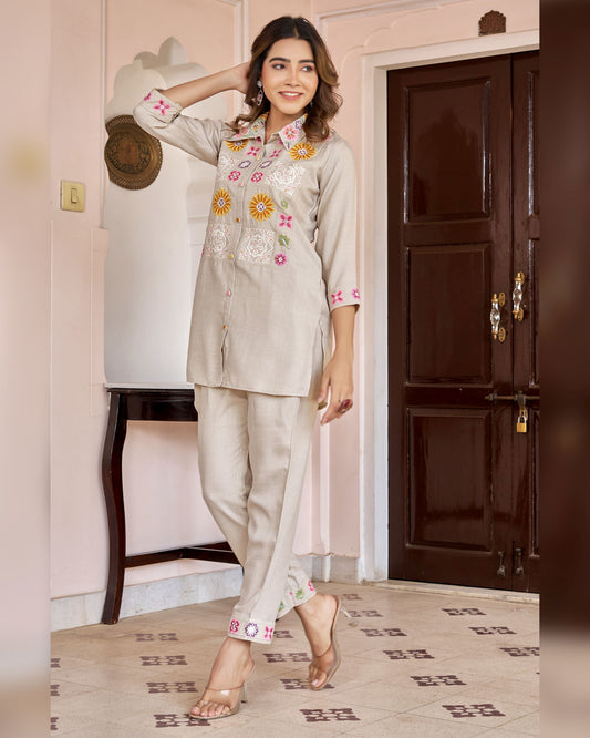 Woman wearing a light gray traditional outfit with floral embroidery in a room.