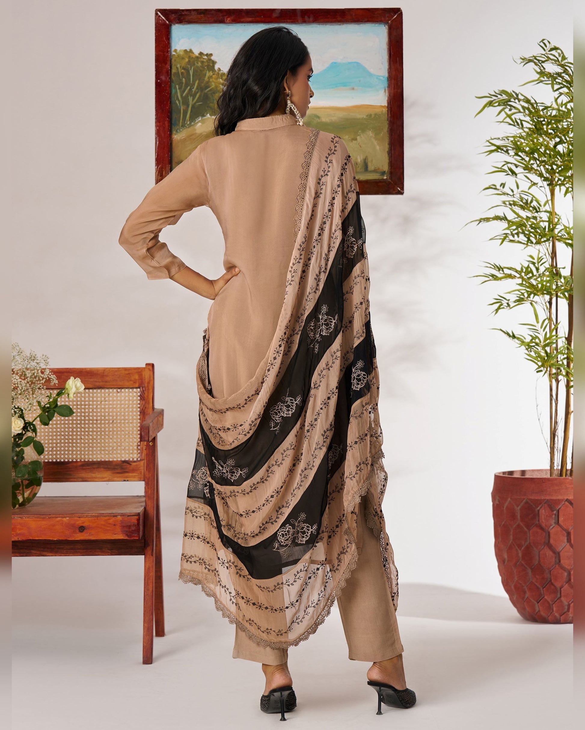 Woman wearing a beige kurta with a black and beige dupatta in a minimalistic room.
