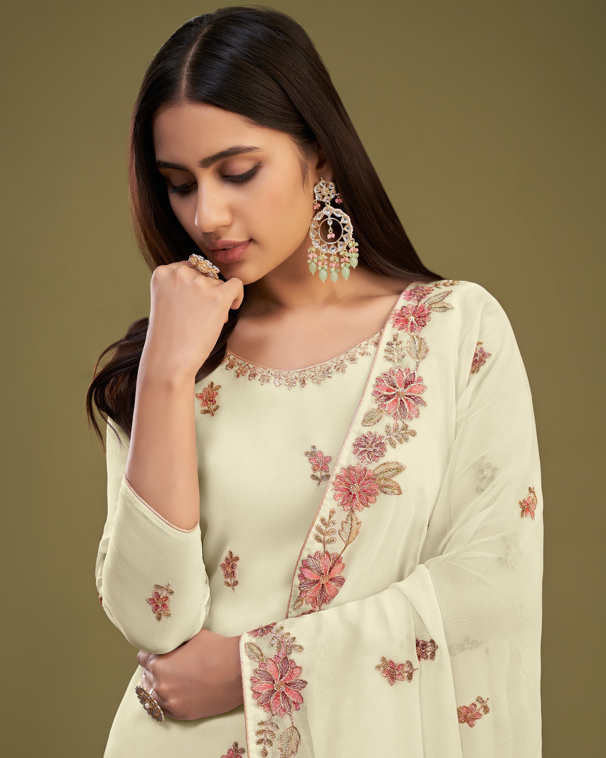 Woman wearing a light green saree with floral embroidery against a brown background
