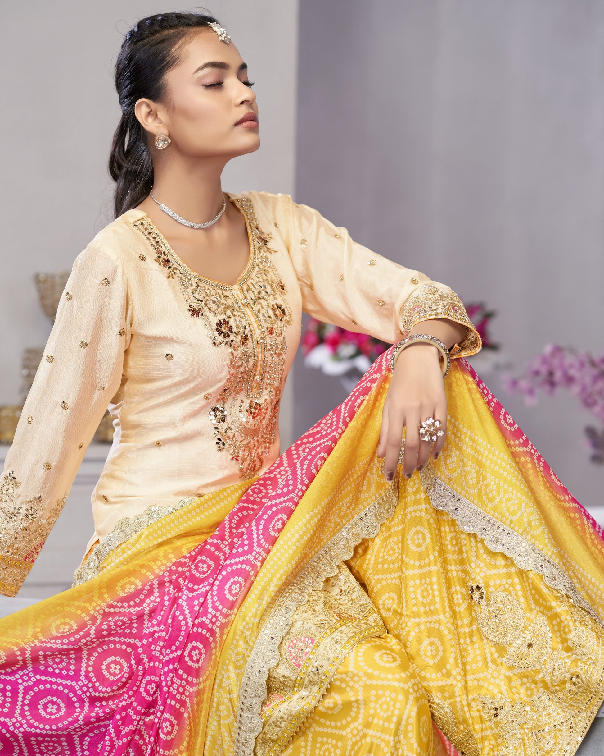 Woman wearing a traditional outfit with a yellow and pink dupatta against a neutral background