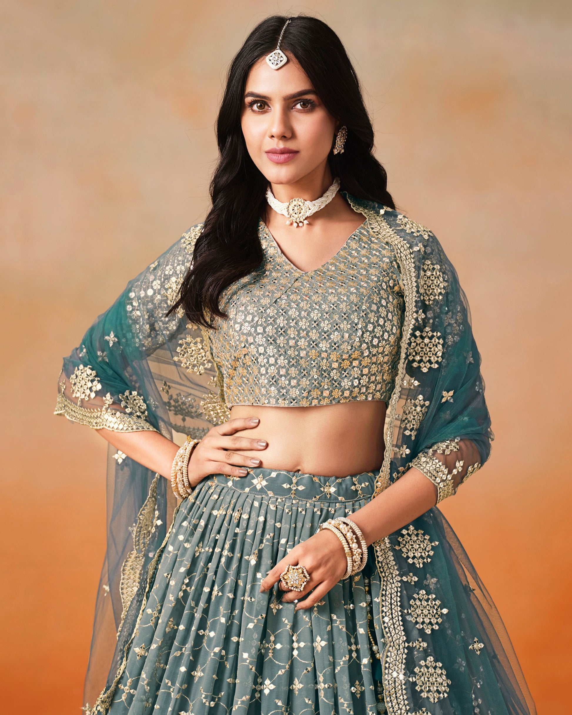 Woman in traditional teal and gold outfit with jewelry against a warm-toned background