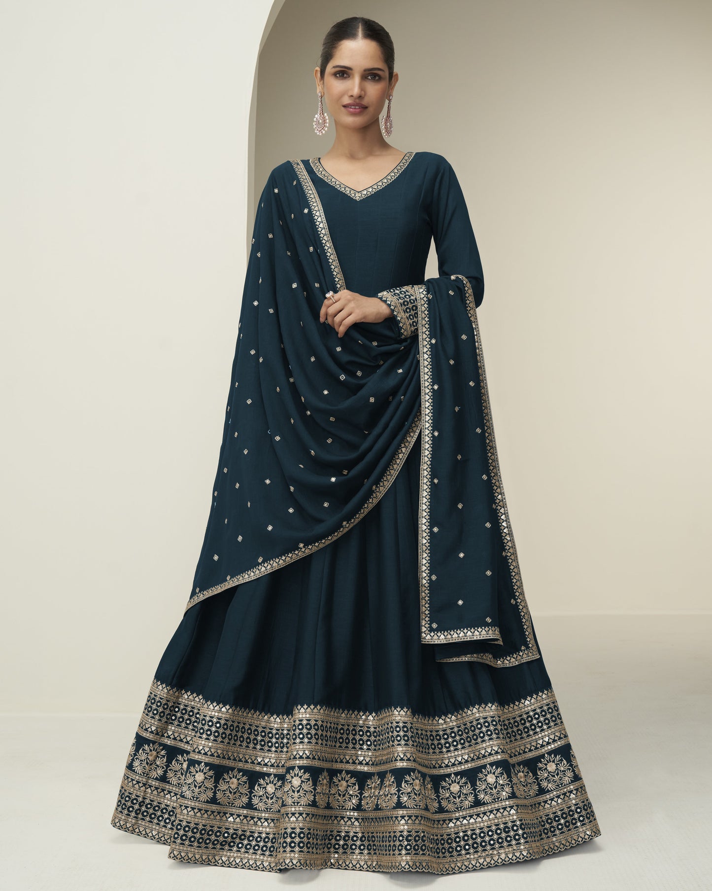 Woman wearing a dark blue traditional outfit with intricate patterns on a neutral background