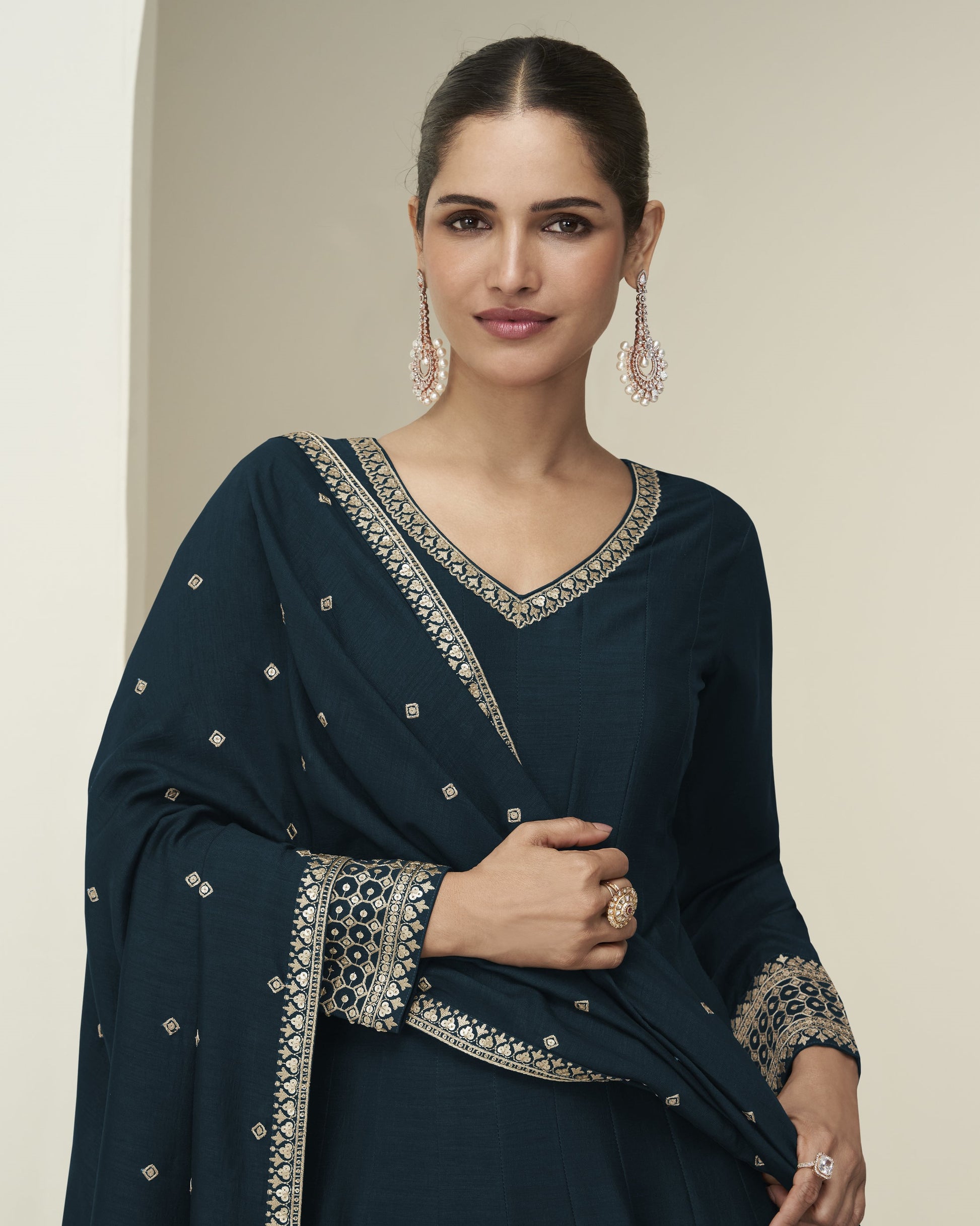 Woman wearing a dark blue embroidered traditional outfit against a neutral background