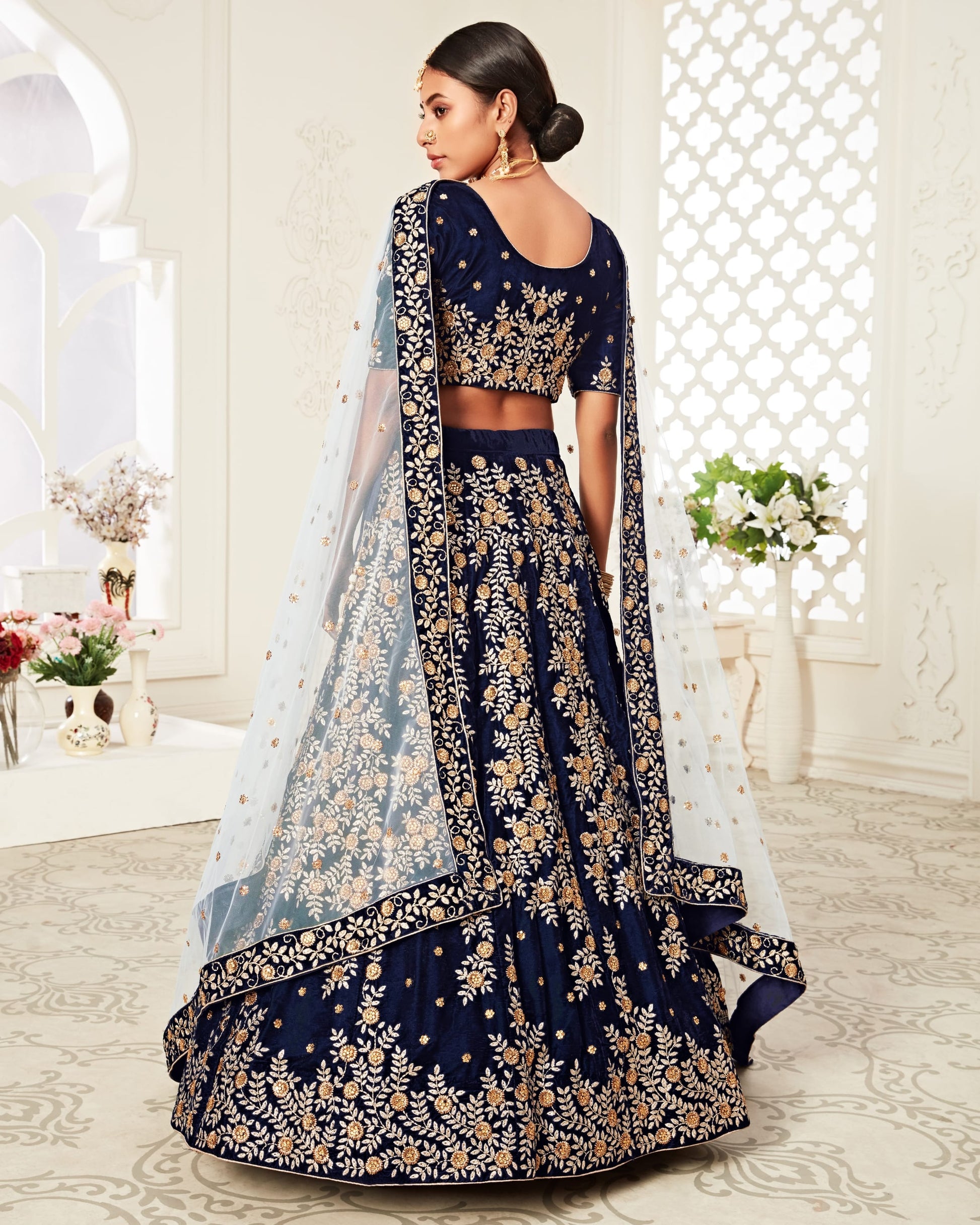 Navy blue embroidered lehenga with gold details in a decorated room.