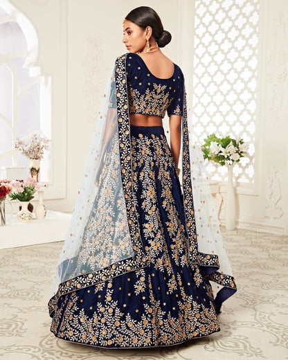 Navy blue embroidered lehenga with gold details in a decorated room.