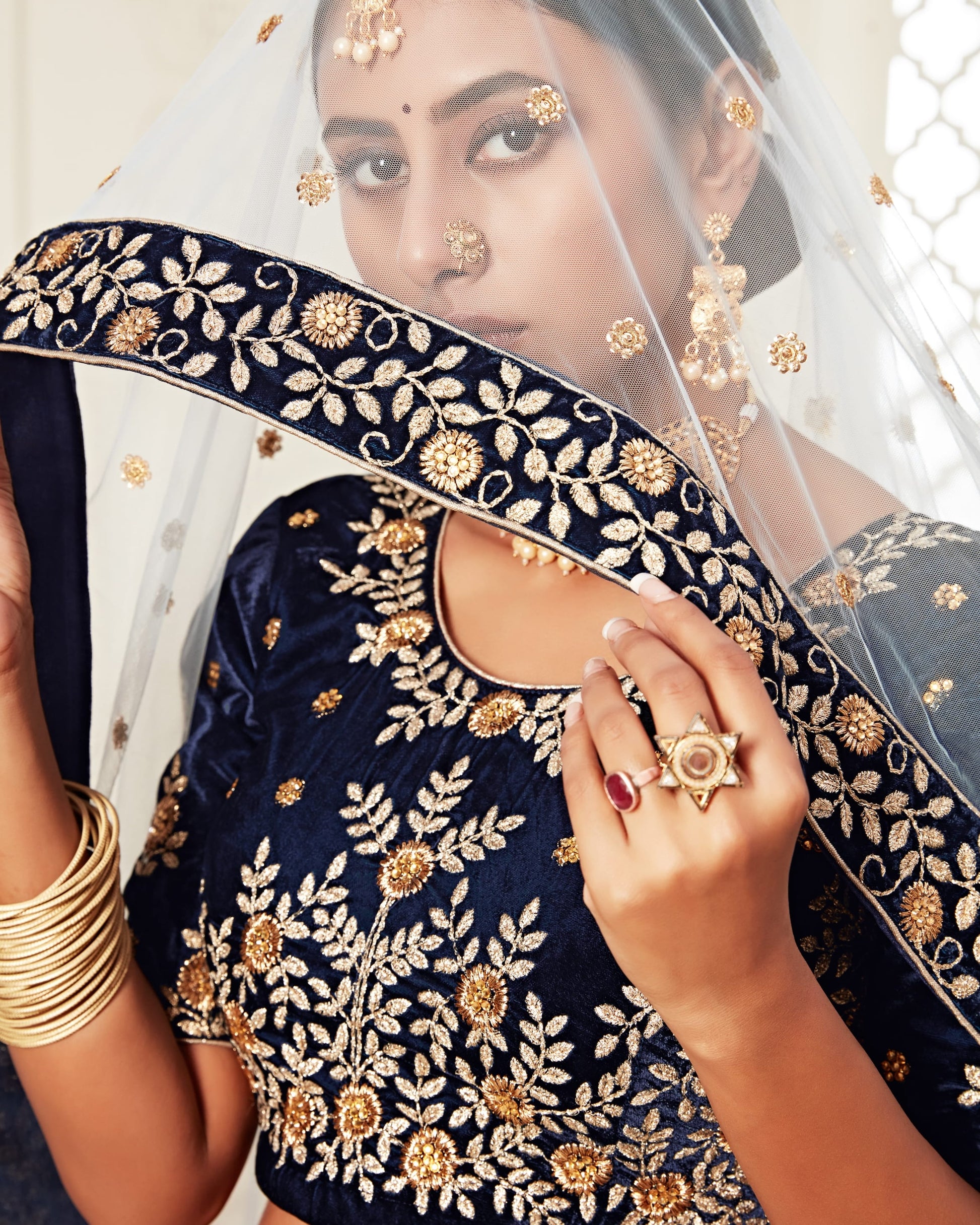 Woman wearing a navy blue embroidered saree with gold details, holding a matching blouse.