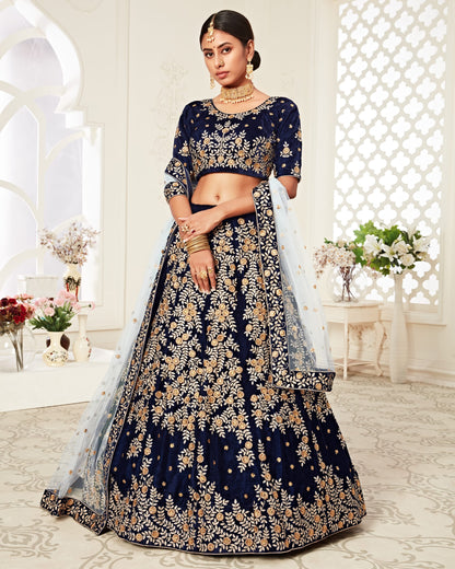 Woman wearing a navy blue embroidered traditional outfit in a decorated room.
