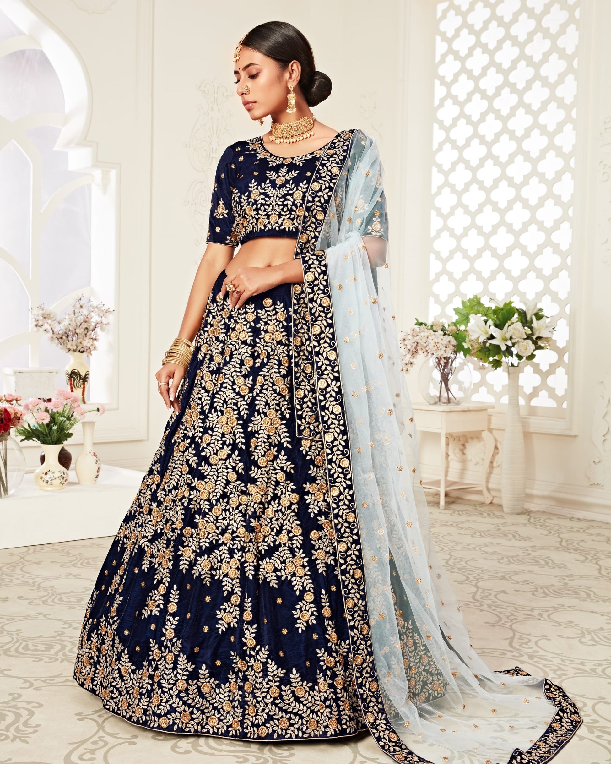 Woman in a navy blue embroidered lehenga with gold details in a decorated room.