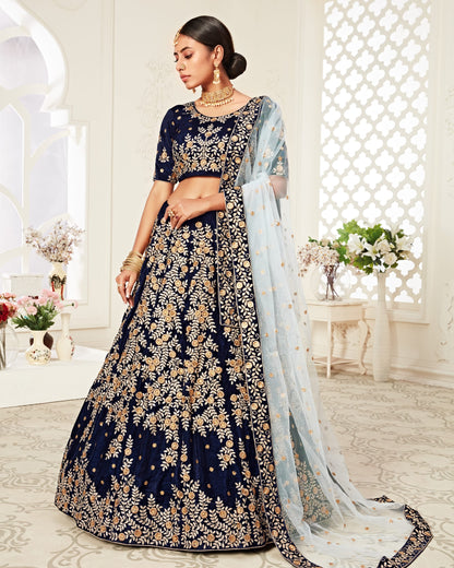 Woman in a navy blue embroidered lehenga with gold details in a decorated room.