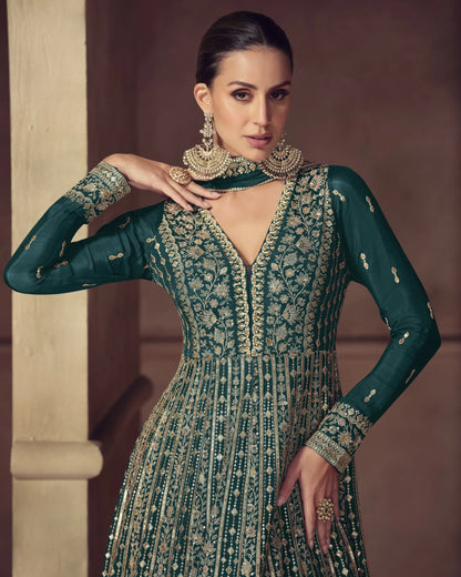 Woman wearing a green and gold embroidered traditional outfit with jewelry against a neutral background