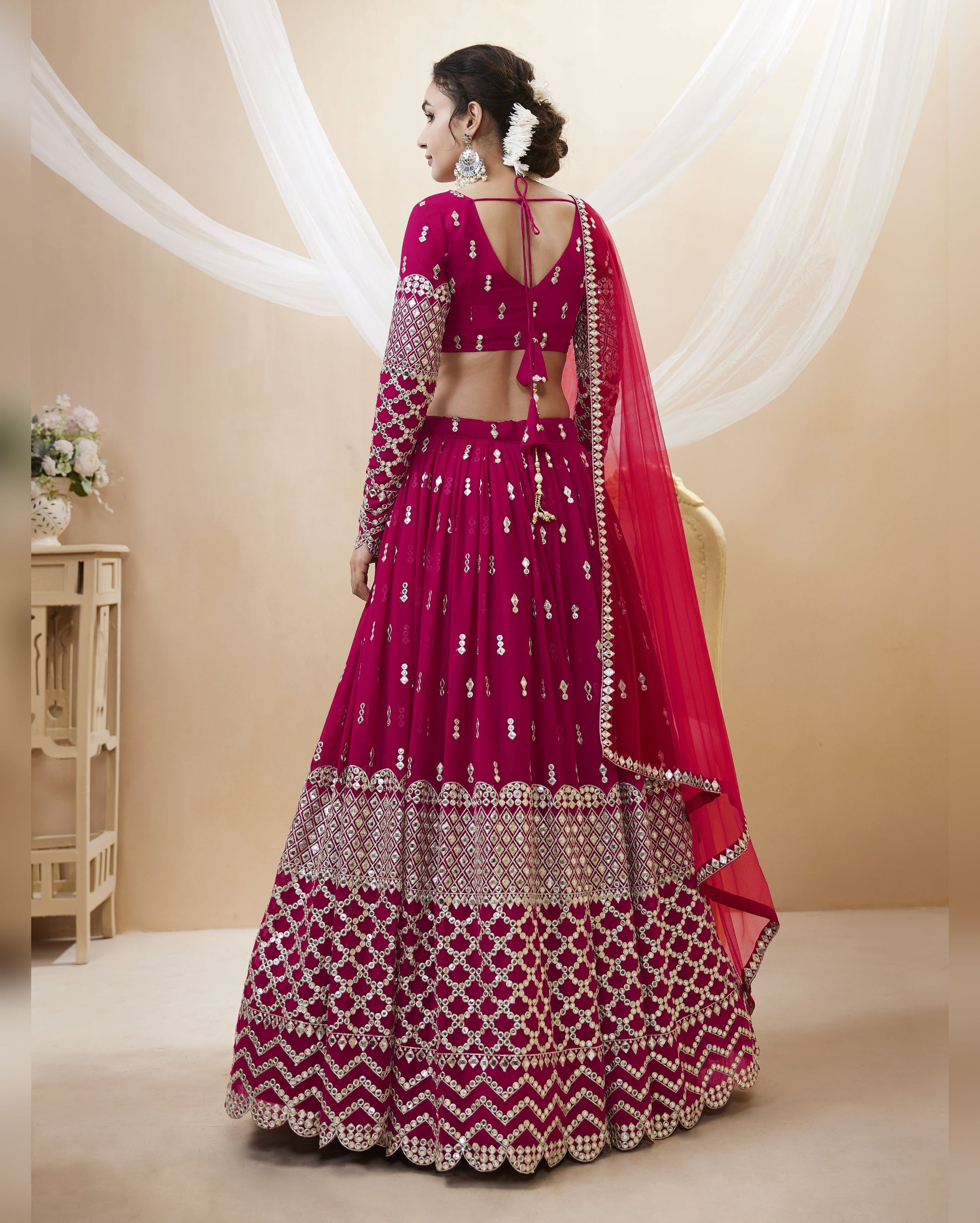 Woman wearing a traditional pink and red lehenga with intricate patterns in a neutral setting.