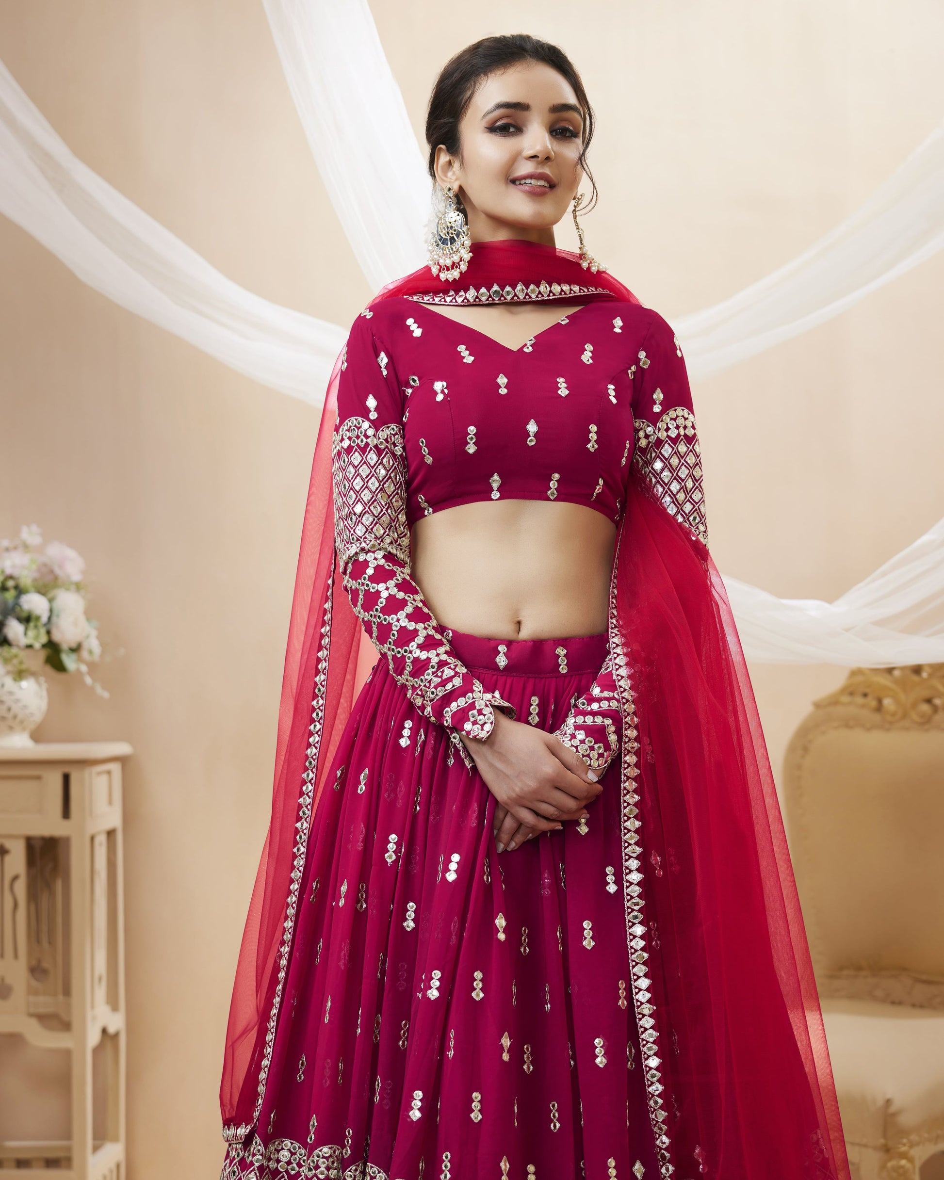 Woman in a maroon traditional outfit with silver embroidery in an elegant indoor setting.