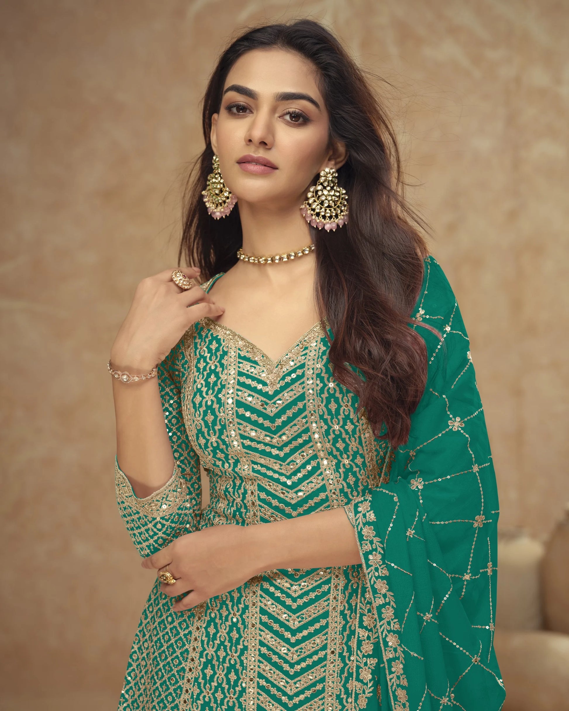 Woman wearing a green and gold traditional outfit with jewelry against a beige background