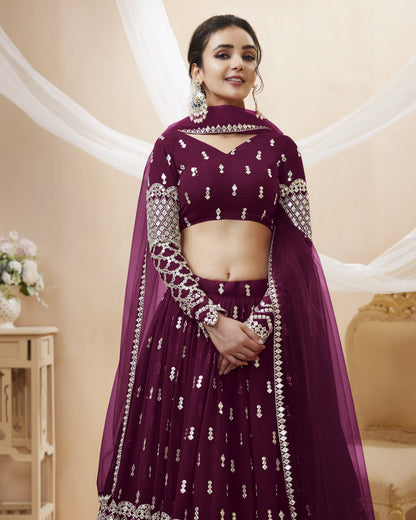 Woman wearing a maroon traditional outfit with white embroidery in a decorated indoor setting.