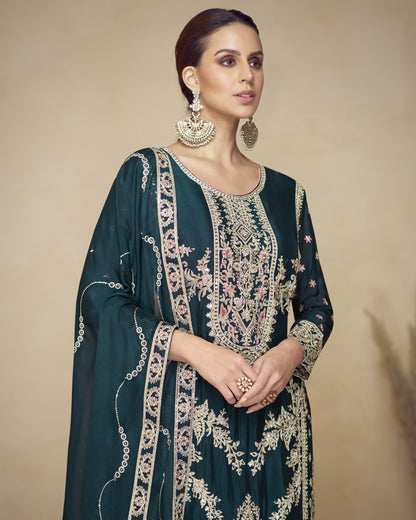 Woman wearing a dark green embroidered traditional outfit with gold jewelry against a beige background