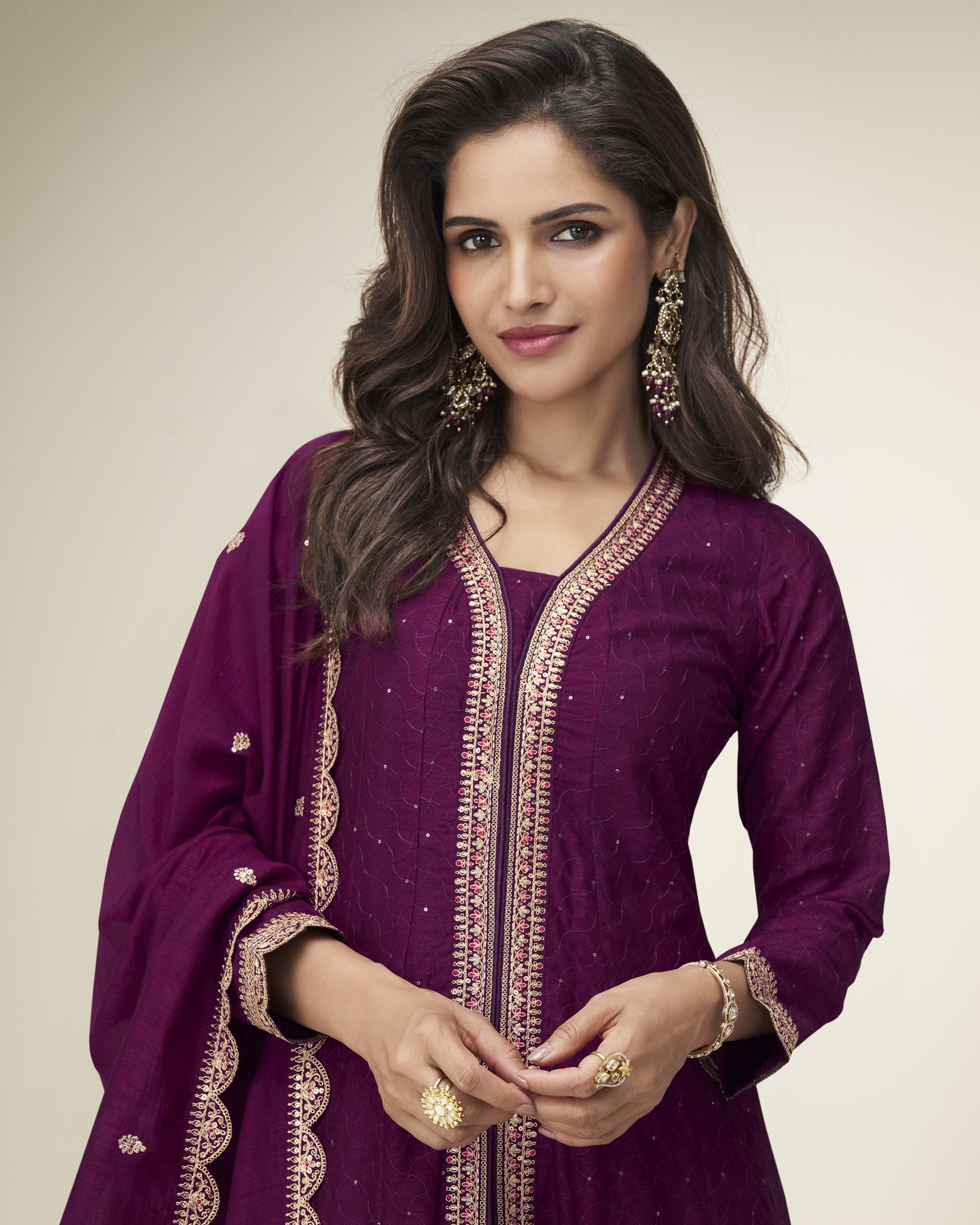 Woman wearing a purple traditional outfit with gold embroidery on a beige background