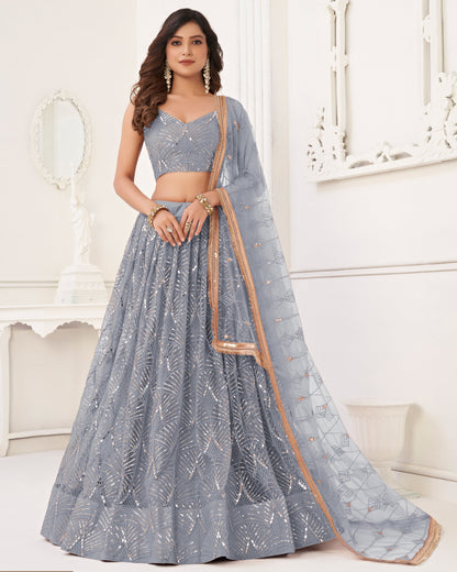 Woman wearing a gray embroidered lehenga with a beige dupatta in a white room.