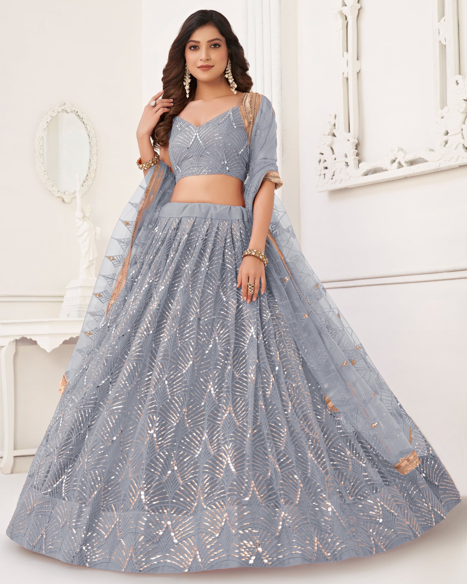 Woman wearing a gray embroidered lehenga with a matching blouse in a white decorated room.