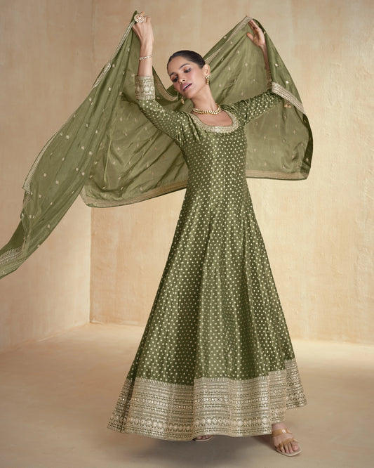 Woman wearing a green traditional outfit with a matching dupatta against a beige background