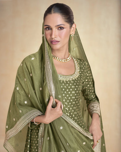 Woman wearing a green traditional outfit with gold embroidery on a beige background