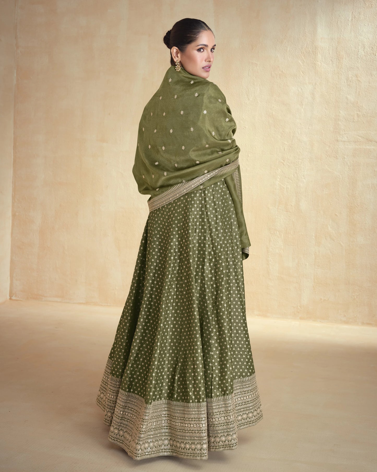 Woman wearing a green traditional outfit with a matching shawl against a beige background