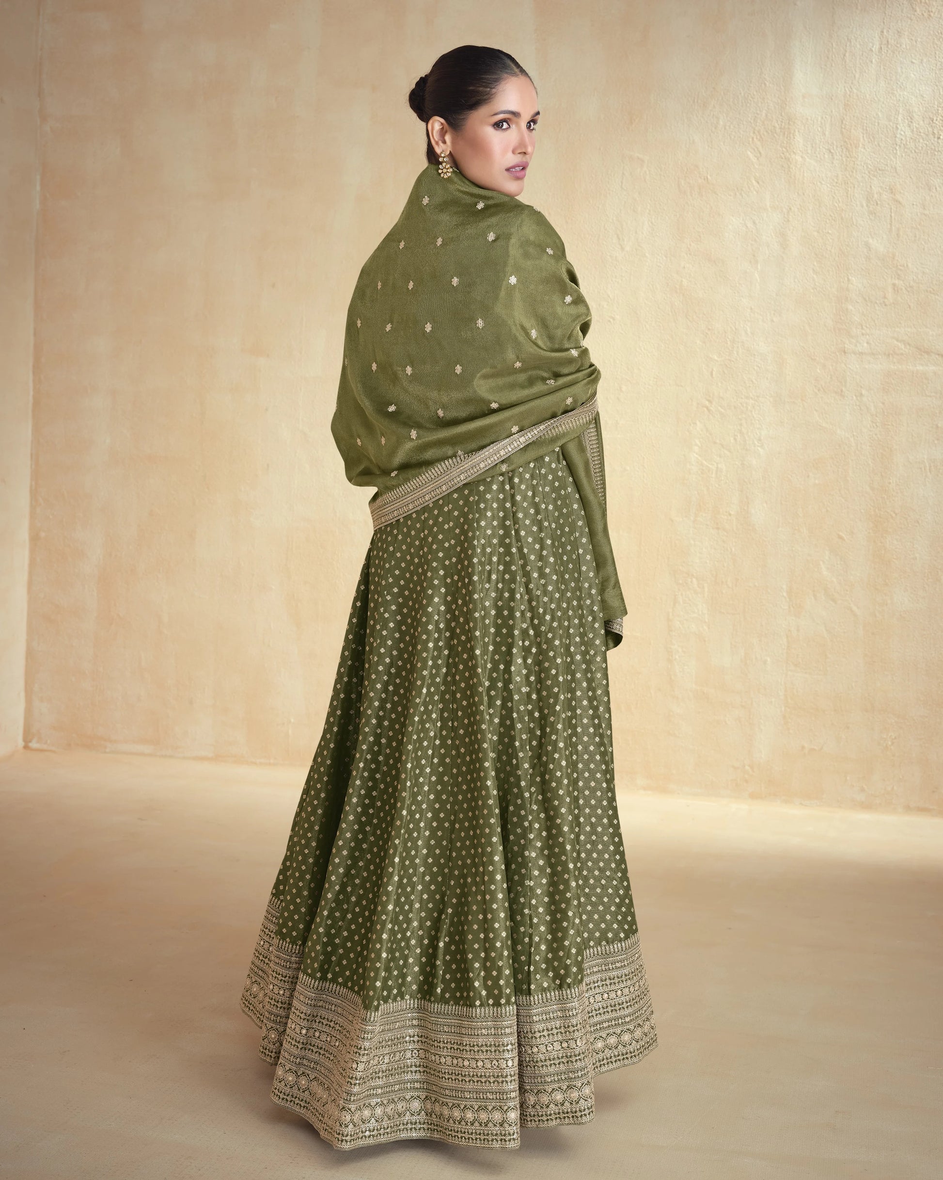Woman wearing a green traditional outfit with a matching shawl against a beige background