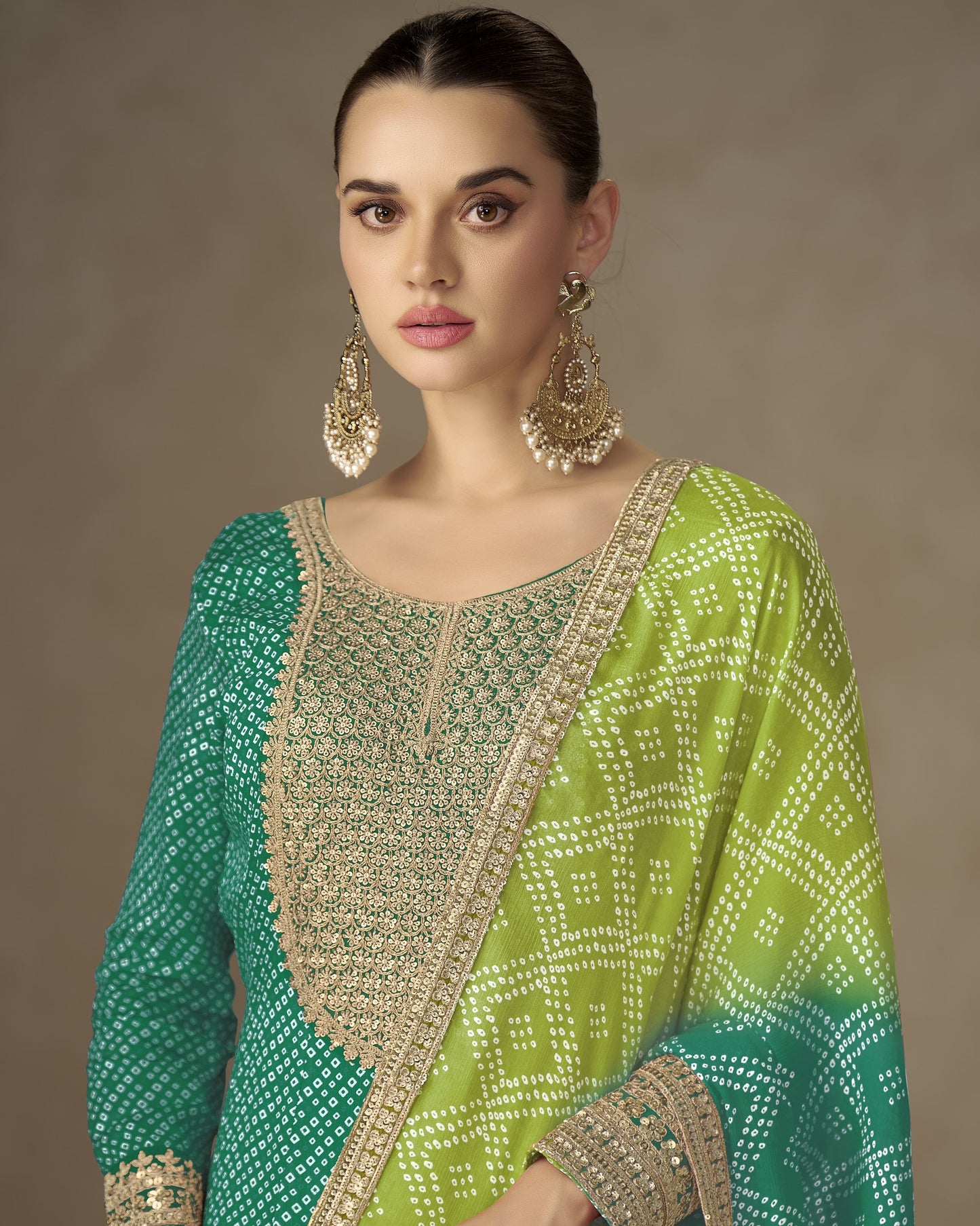 Woman wearing a green and blue traditional outfit with intricate patterns and jewelry against a neutral background