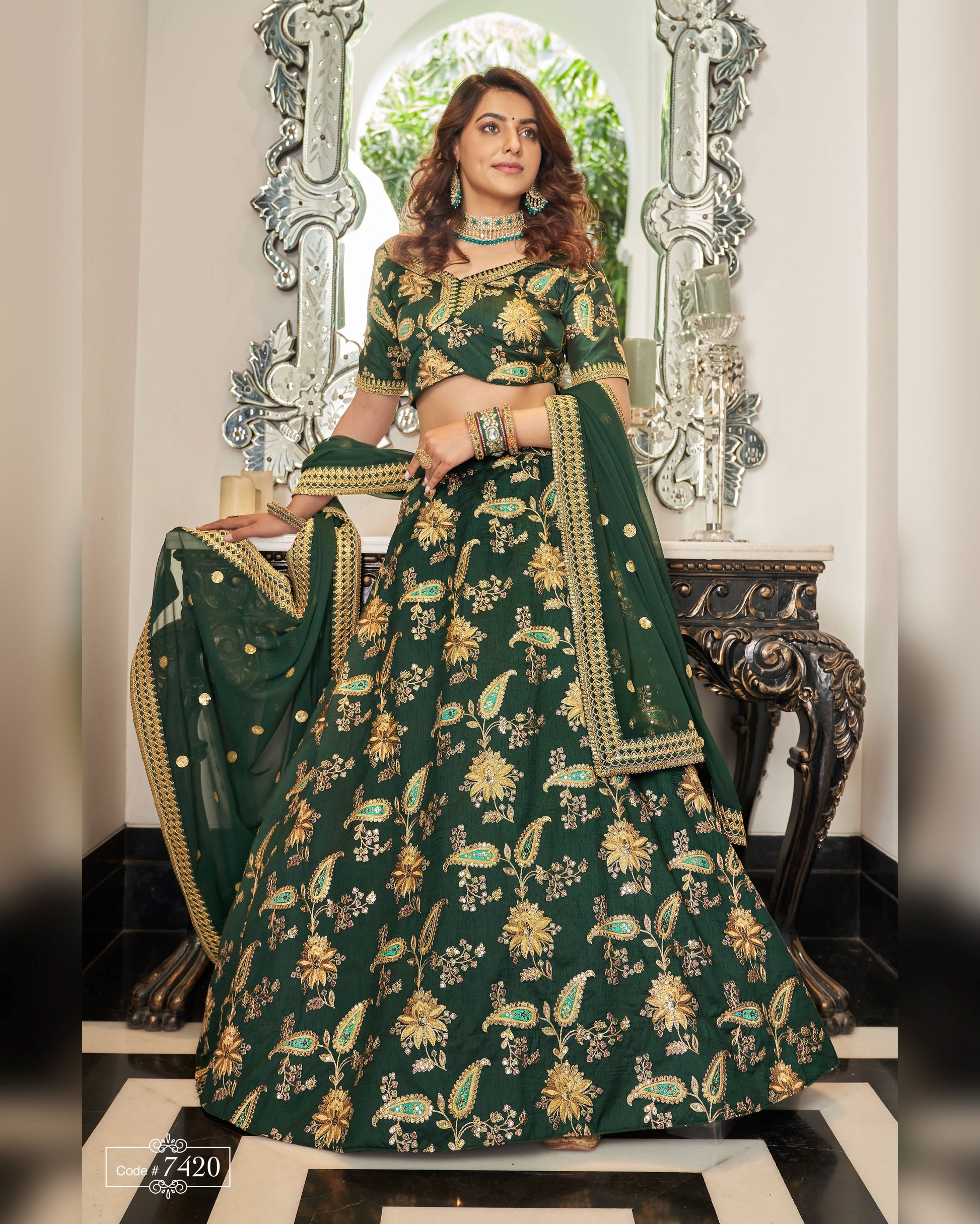 Woman in a green embroidered traditional outfit standing in front of decorative mirrors.