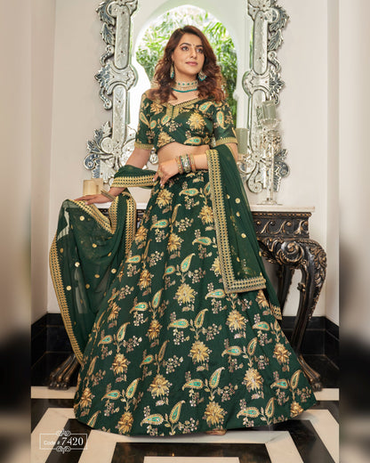 Woman in a green embroidered traditional outfit standing in front of decorative mirrors.