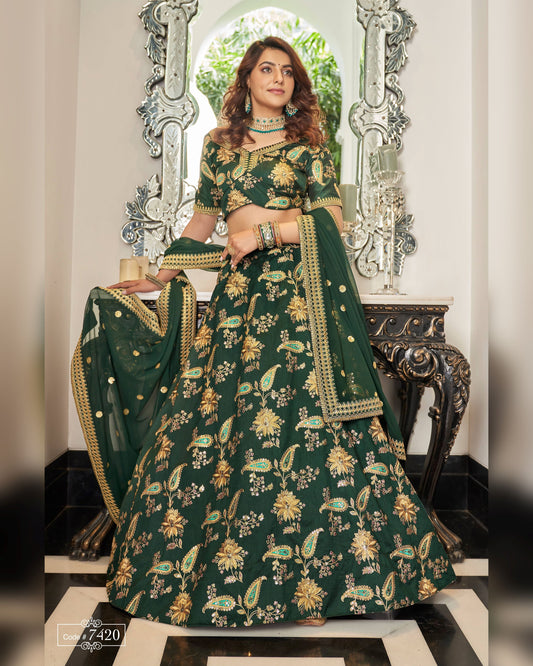 Woman in a green embroidered traditional outfit standing in front of decorative mirrors.