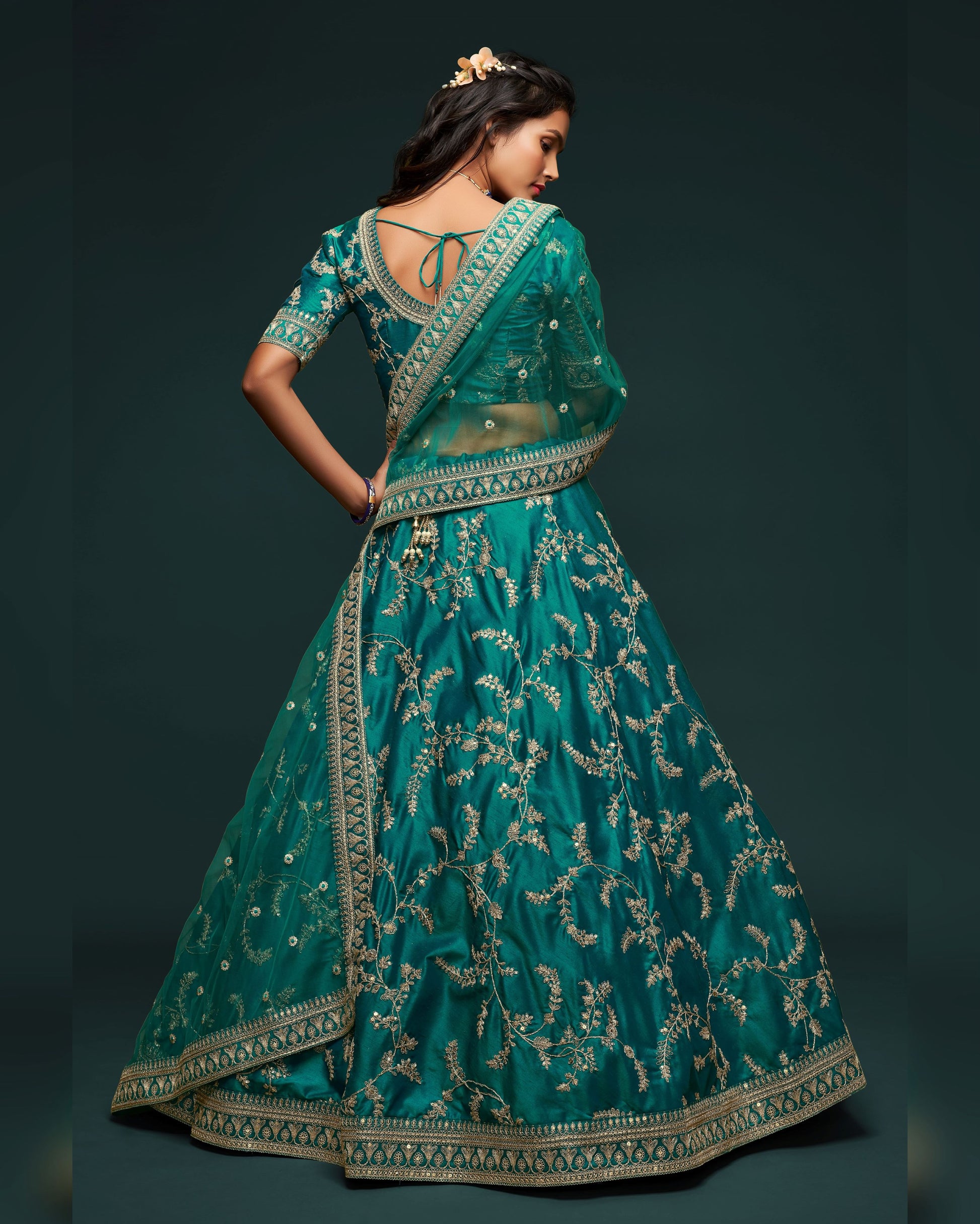 Teal embroidered traditional outfit with gold detailing on a dark background