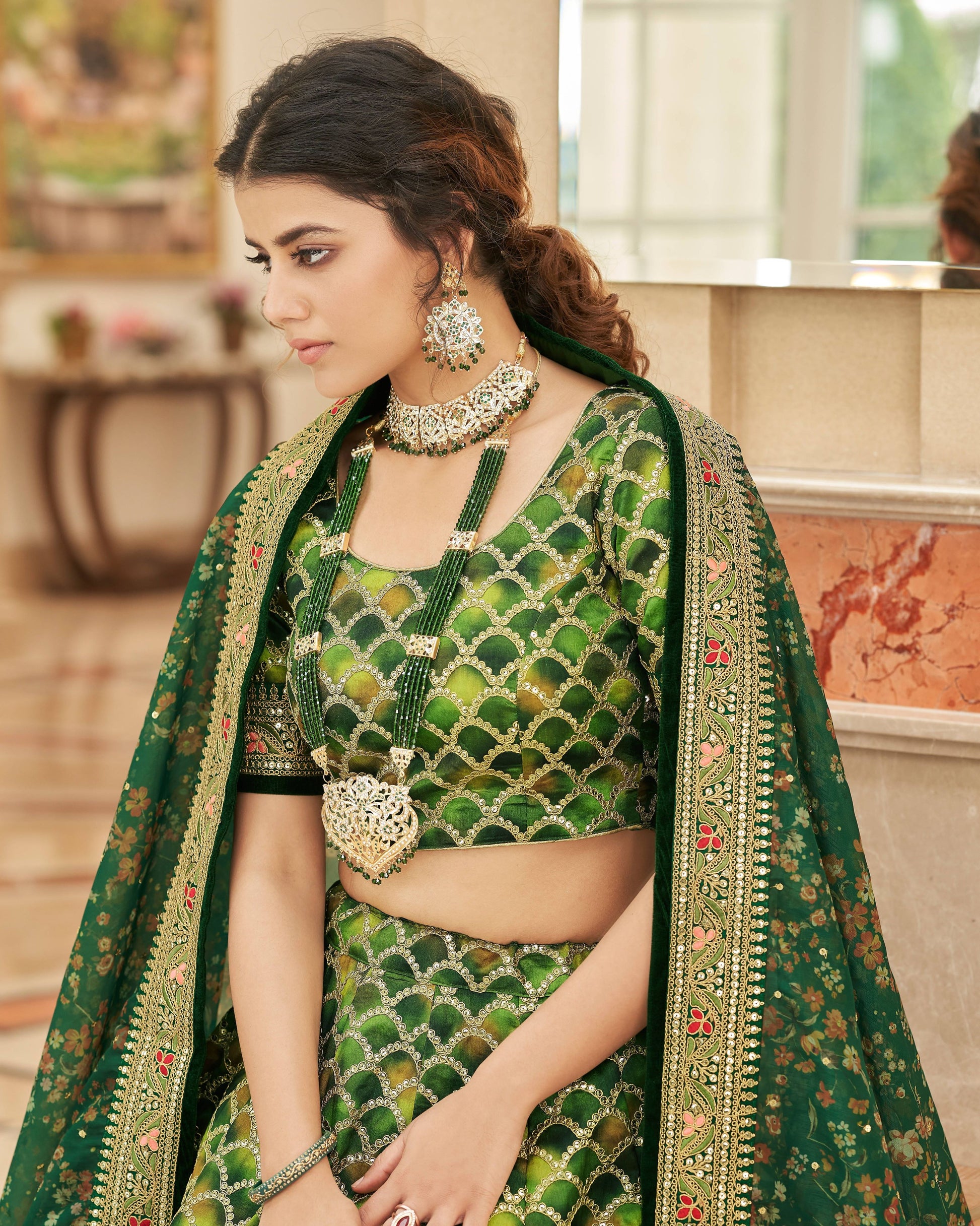 Woman wearing a green embroidered traditional outfit with jewelry indoors.