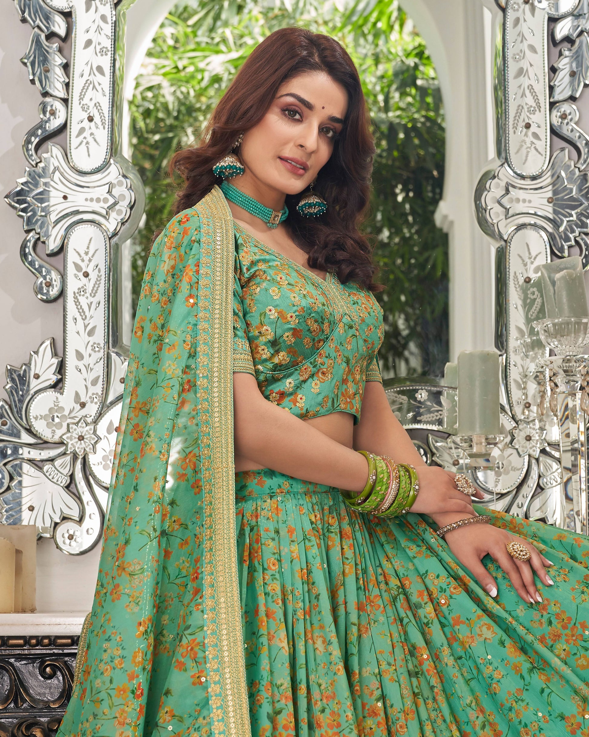 Woman in a green floral saree standing in front of decorative mirrors.
