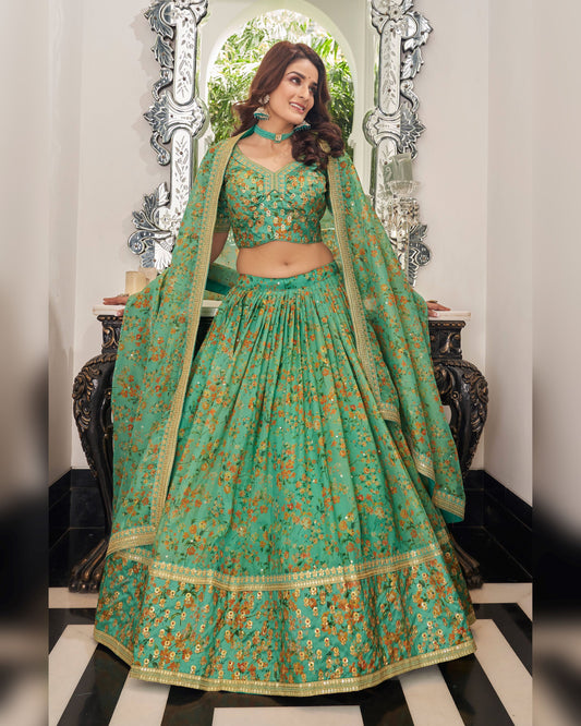 Woman in a traditional green and gold outfit with floral patterns, standing in front of a decorative mirror.